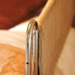 a bed with a white blanket and a silver metal bed handle at Havendale Accessible Holiday Cottage