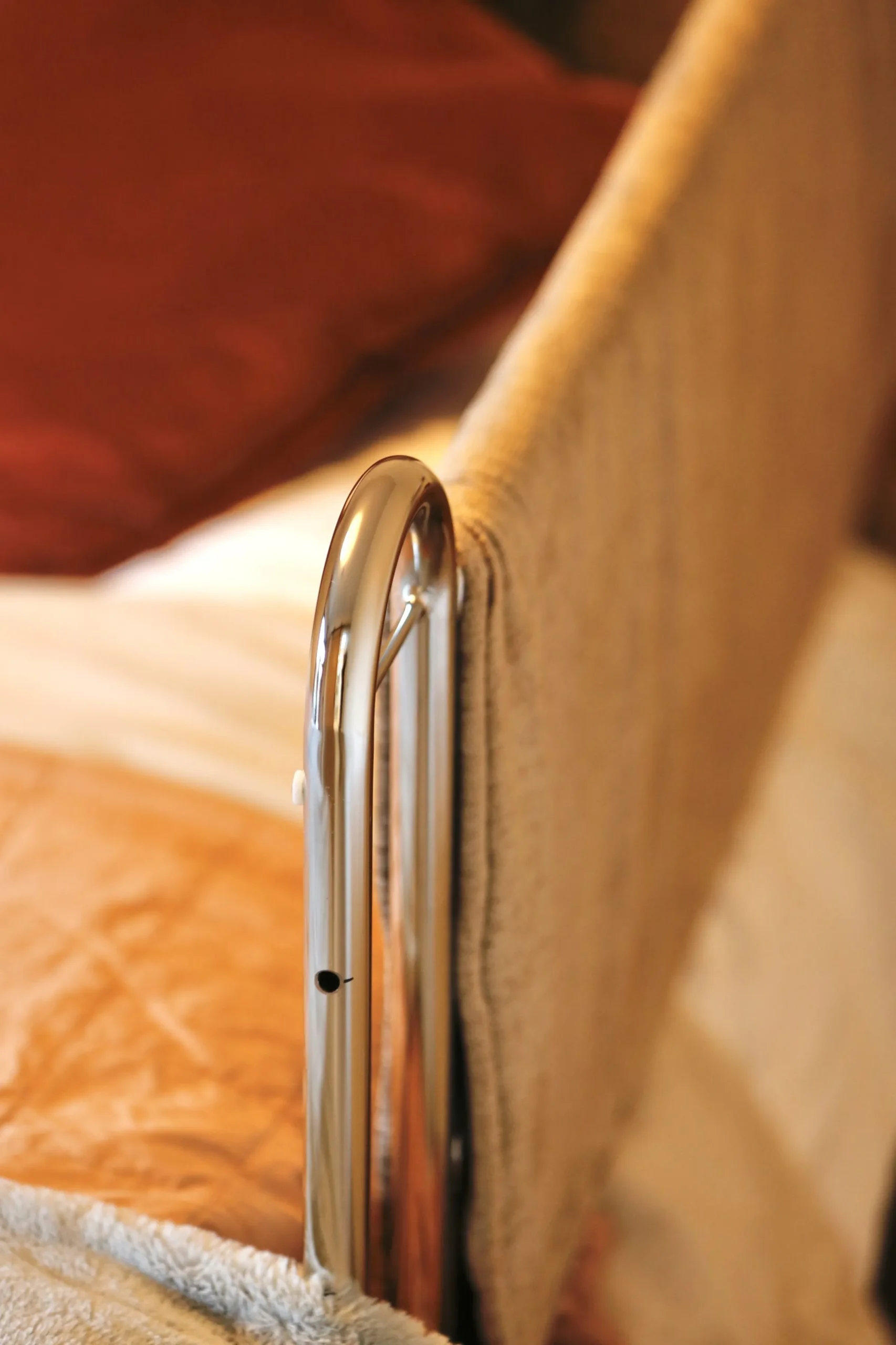 a bed with a white blanket and a silver metal bed handle at Havendale Accessible Holiday Cottage