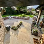 a patio with a stone wall and the garden at Havendale Accessible Holiday Cottage